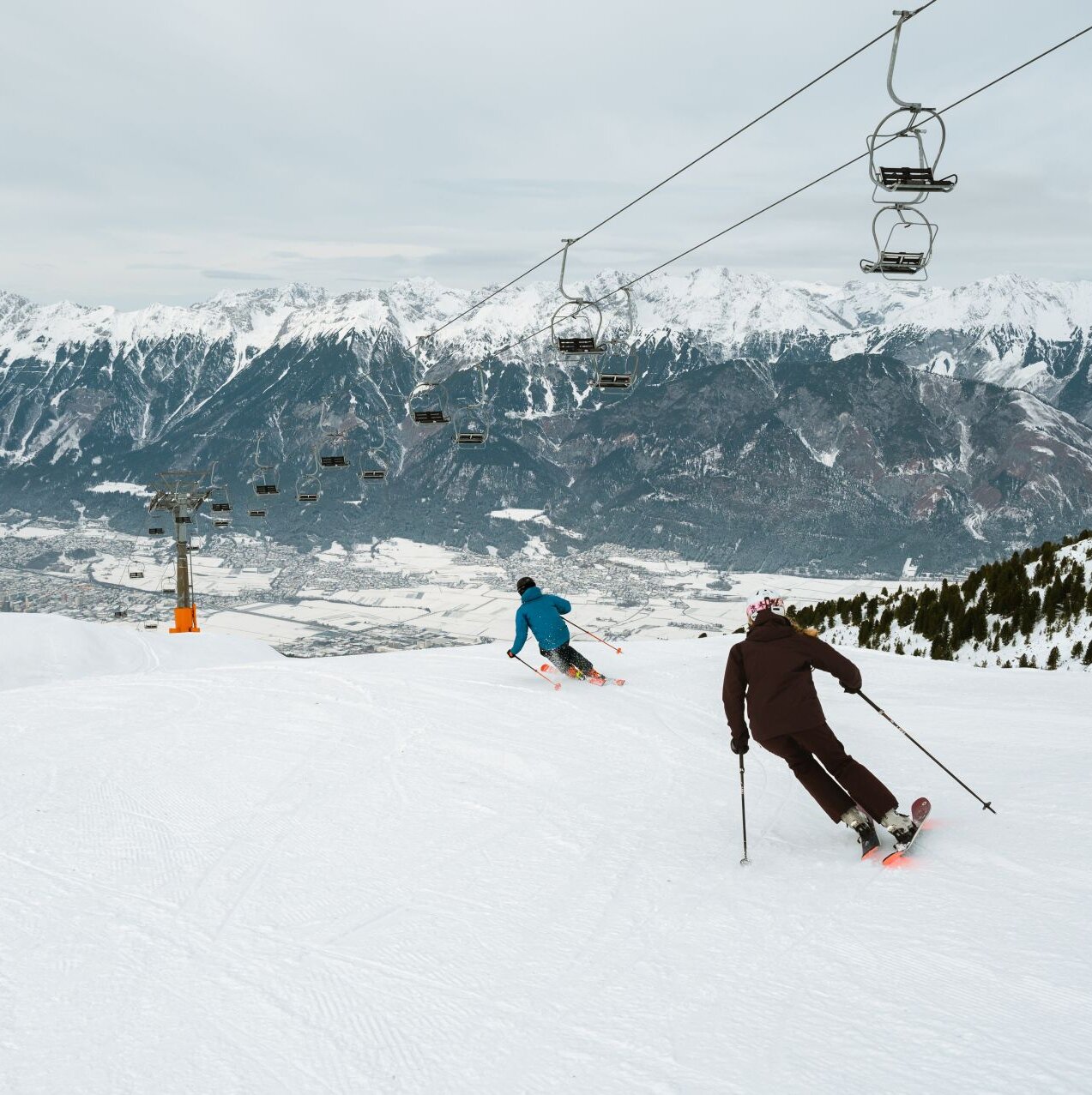 Zwei Skifahrer fahren unter einem Sessellift.