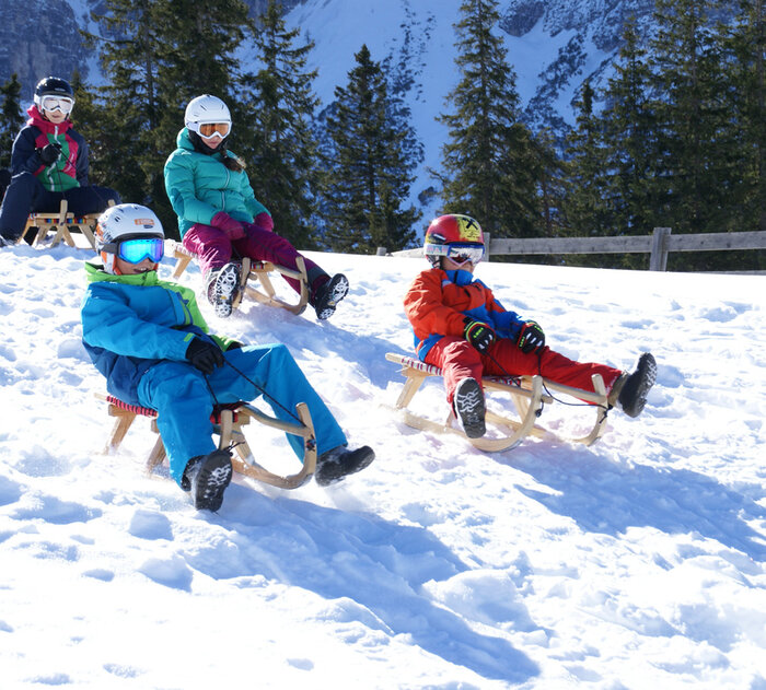 Kinder fahren auf Rodeln eine Piste hinunter.