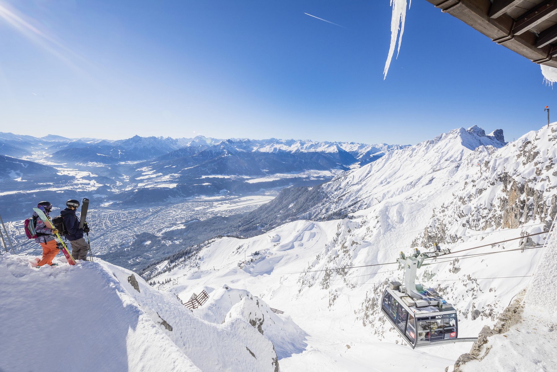 Zwei Wintersportler am Hafelekar mit blick auf Innsbruck und die einfahrende Gondel